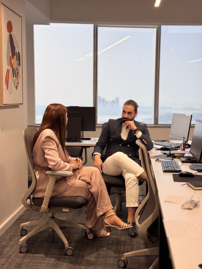 about-me Two professionals in a modern office, discussing business strategies by large windows.